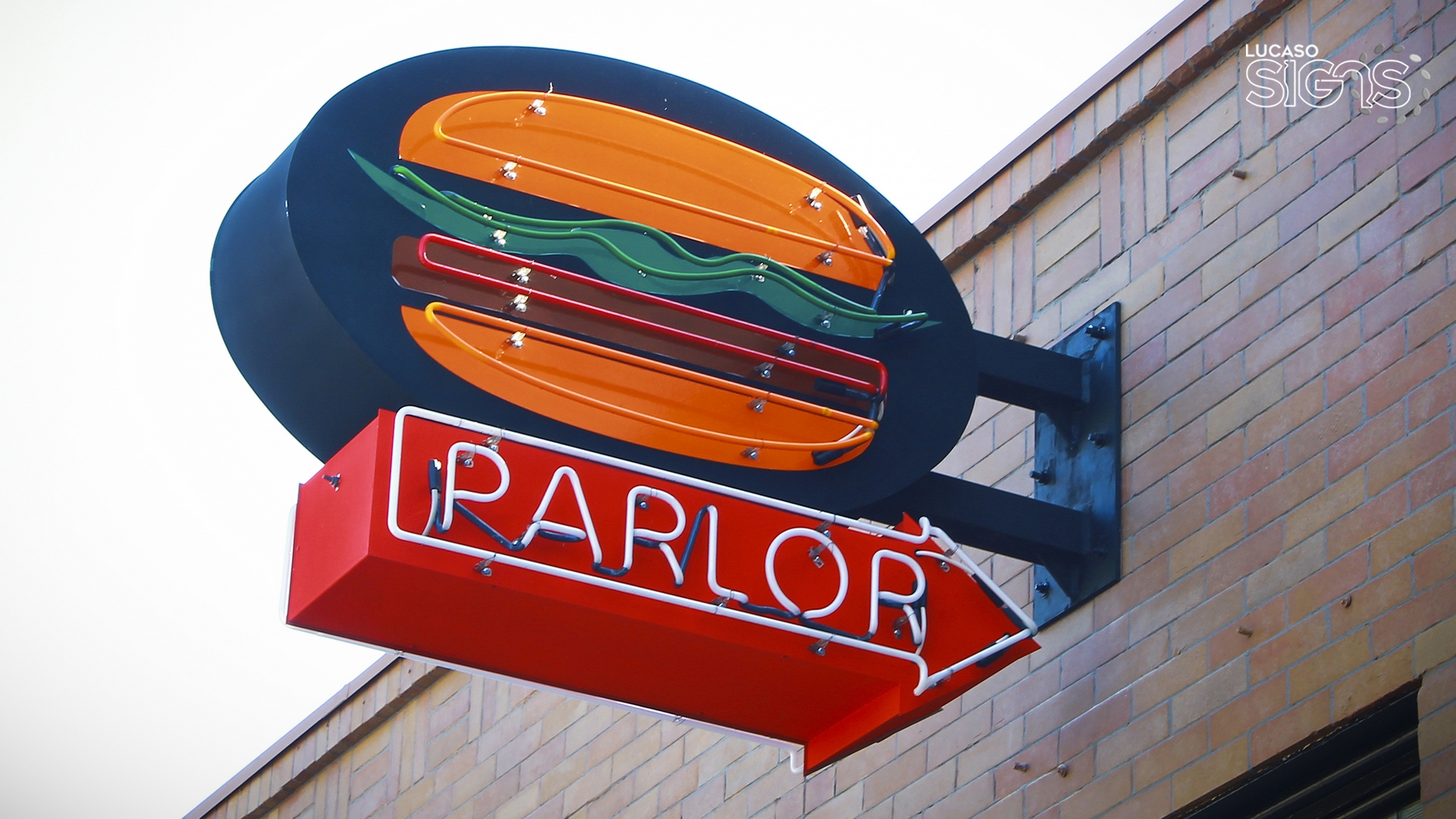 Custom blade sign with neon burger graphic and illuminated PARLOR text mounted on brick wall by Lucaso Signs