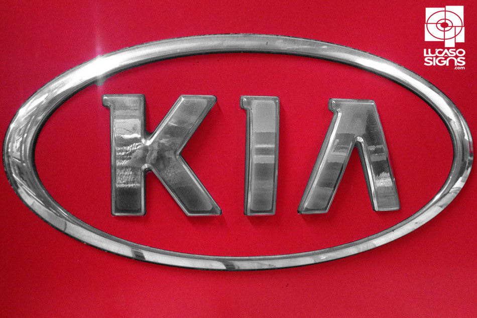 Chrome thermoformed 3D KIA emblem with raised letters and oval border on red background, custom made by Lucaso Signs